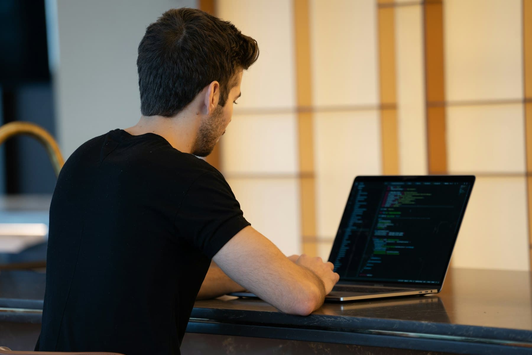 A developer in a black t-shirt writing code on a laptop in warm evening light