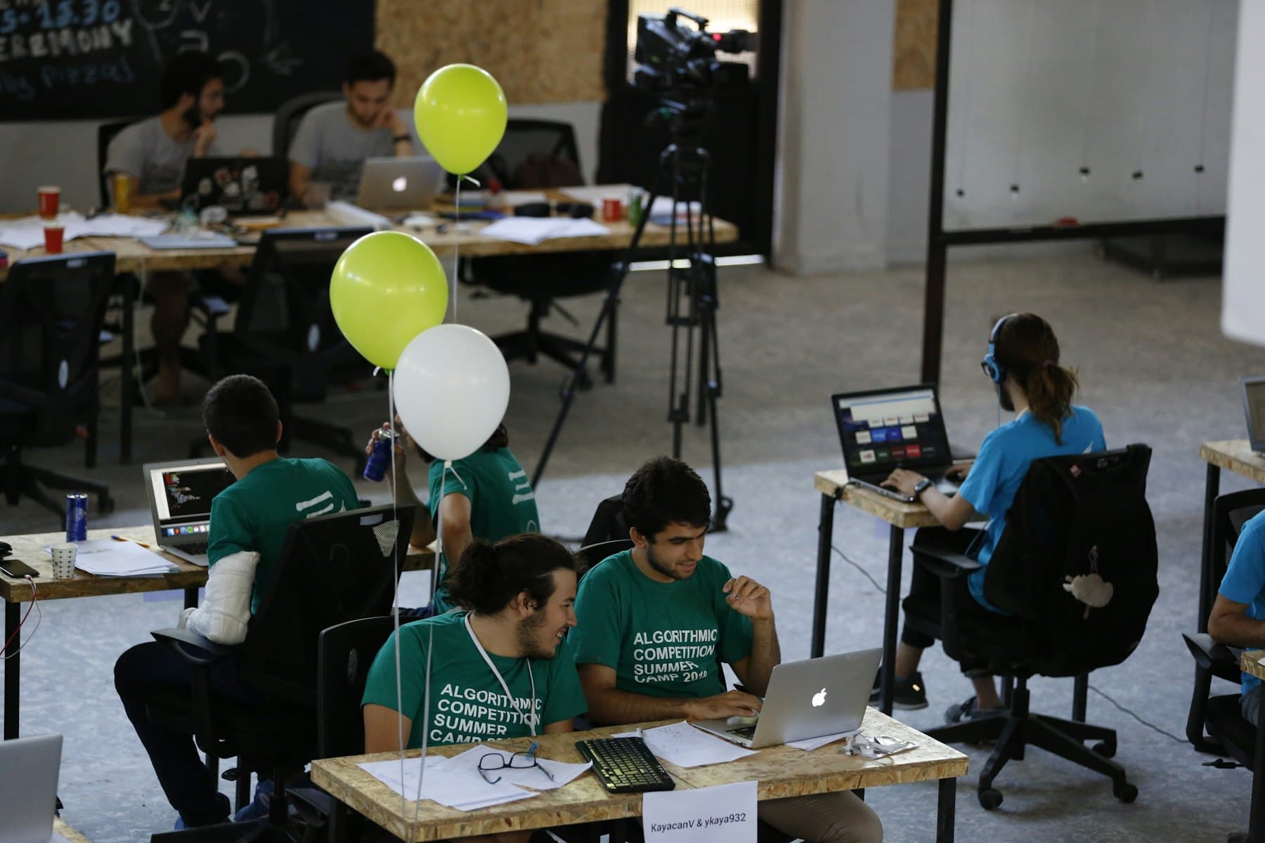 Des étudiants en t-shirts assortis travaillent sur des portables à de longues tables pendant une compétition de programmation